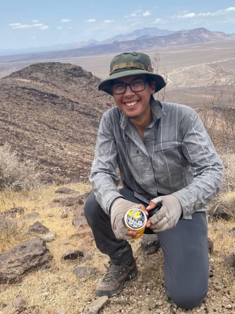 Jose Torres in a desert landscape holding jar of vials